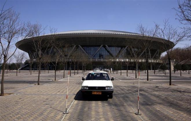 A car driven by a student of a driving school slowly moves around the carpark in front of the deserted 2008 Beijing Olympics venue for the cycling competition in central Beijing